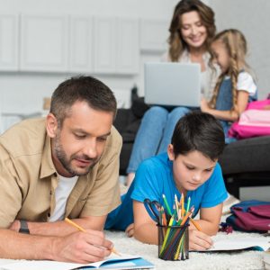 selective focus of father and son doing homework together while mother and daughter using laptop on